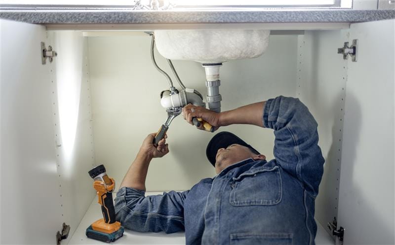 Plumber repairing pipes beneath a bathroom sink in Petaluma